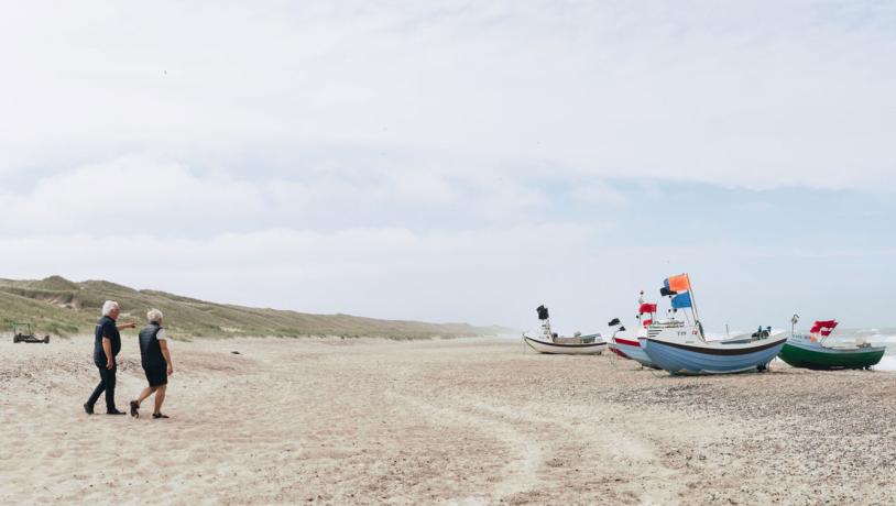 Two people take a walk beside boats on the beach at Snedsted, Thy National Park