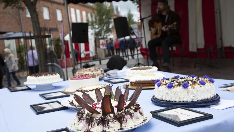 Bild von einem Tisch mit Kuchen und im Hintergrund einer Szene, Kuchenfestival in Sønderjylland 2021