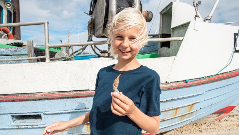 Ein Bild von einem Kind vor einem Fischerboot am Strand in Thorupstrand