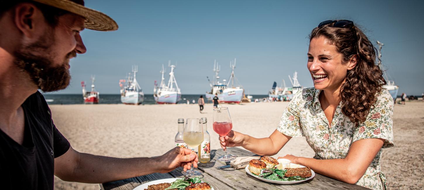 A couple eating fish at Thorup Strand with the sea and boats in the background