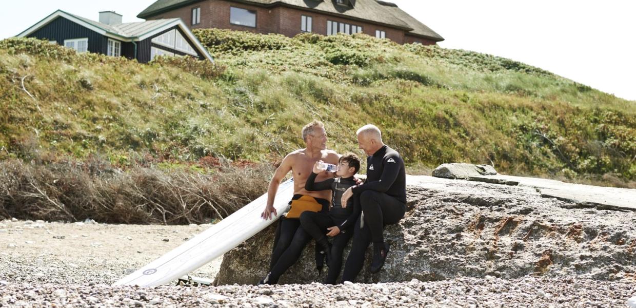 Two men and a child play on a beach beside a summerhouse in Denmark