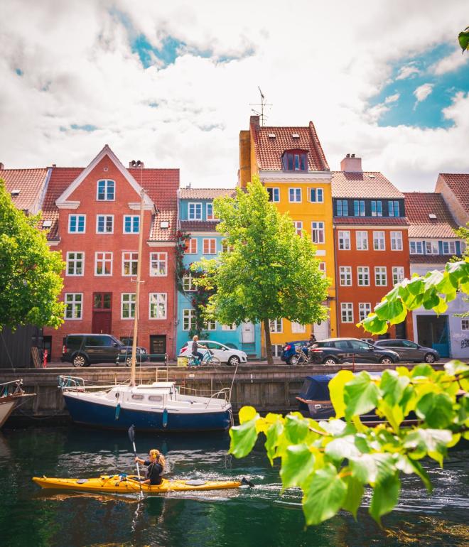 Kvinne i kayakk forbi fargerike kanaler i Christianshavn