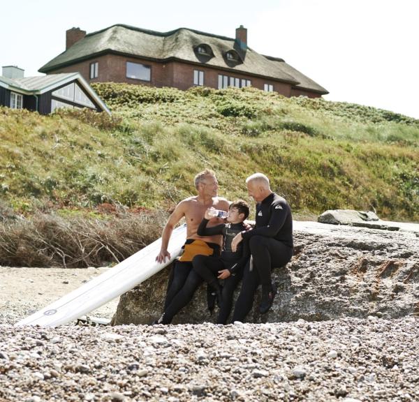 Two men and a child play on a beach beside a summerhouse in Denmark