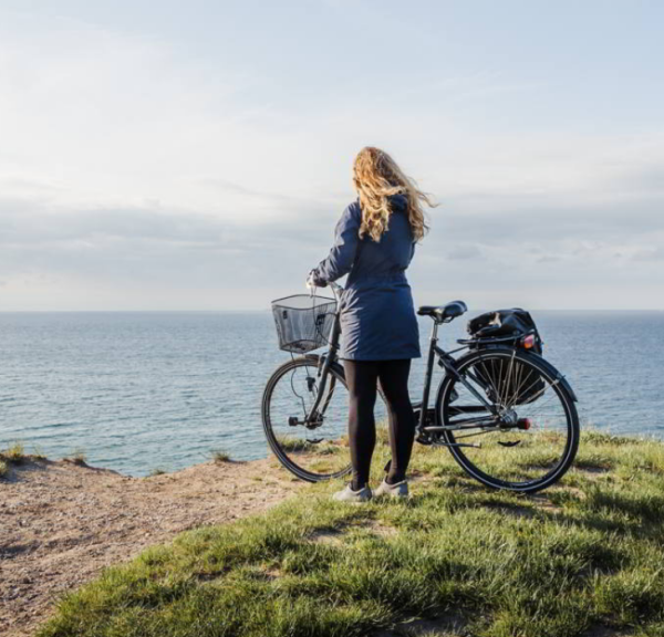 Frau mit Fahrrad schaut aufs Meer, Nordkyststien in Dänemark