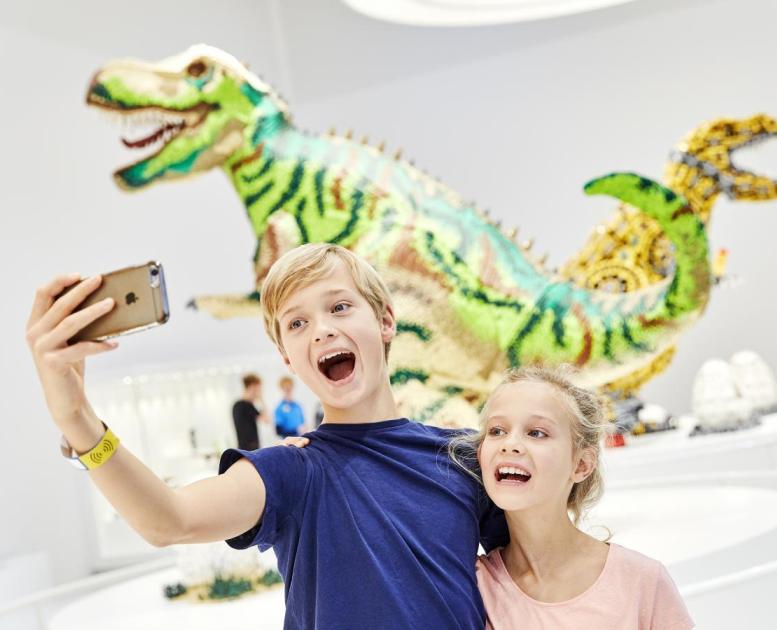 Geschwister machen ein Selfie vor den LEGO Dinosauriern im LEGO House in Billund