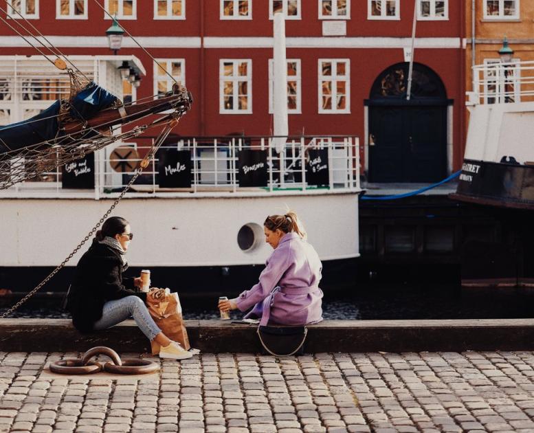 To kvinner sitter ved Nyhavn i København