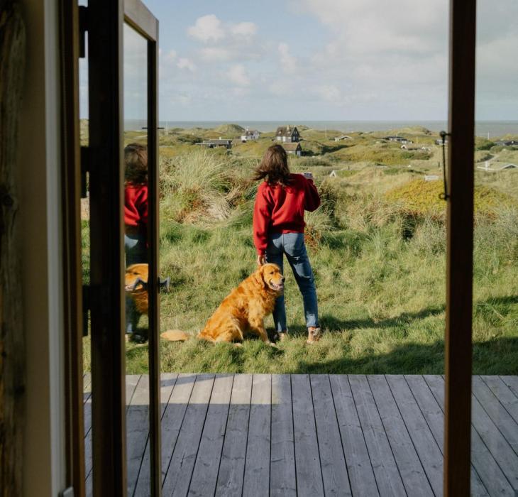 Frau mit Hund auf der Terasse eines Ferienhauses an der dänischen Westküste